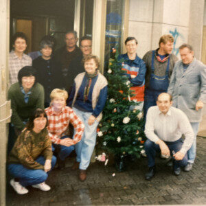 Ein Bild von einer Gruppe von Menschen. Männer und Frauen stehen vor dem Frauen-Zentrum. Ein Weihnachts-Baum ist in der Mitte. Das Bild ist 25 Jahre alt, also von 1997