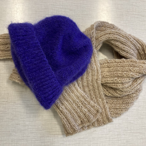 Ein Foto von einem Schal und einer Mütze. Schal und Mütze sind aus Strick. Die Mütze ist blau. Der Schal ist braun.