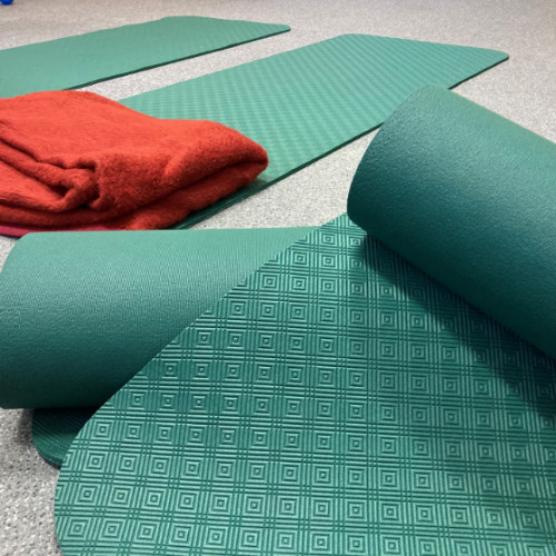 Ein Foto von 4 grünen Gymnastik-Matten. Die Matten liegen auf dem Boden. Eine rote Decke liegt auf einer Matte.